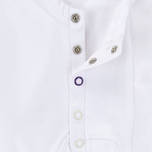 May include: White baby onesie with a row of silver snaps down the front.