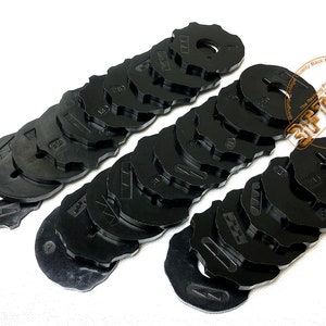 Puede incluir: Un juego de 20 pies prensatelas de máquina de coser de plástico negro, cada uno con un tamaño y una forma diferentes. Los pies están dispuestos en dos filas, con los tamaños más pequeños a la izquierda y los tamaños más grandes a la derecha.