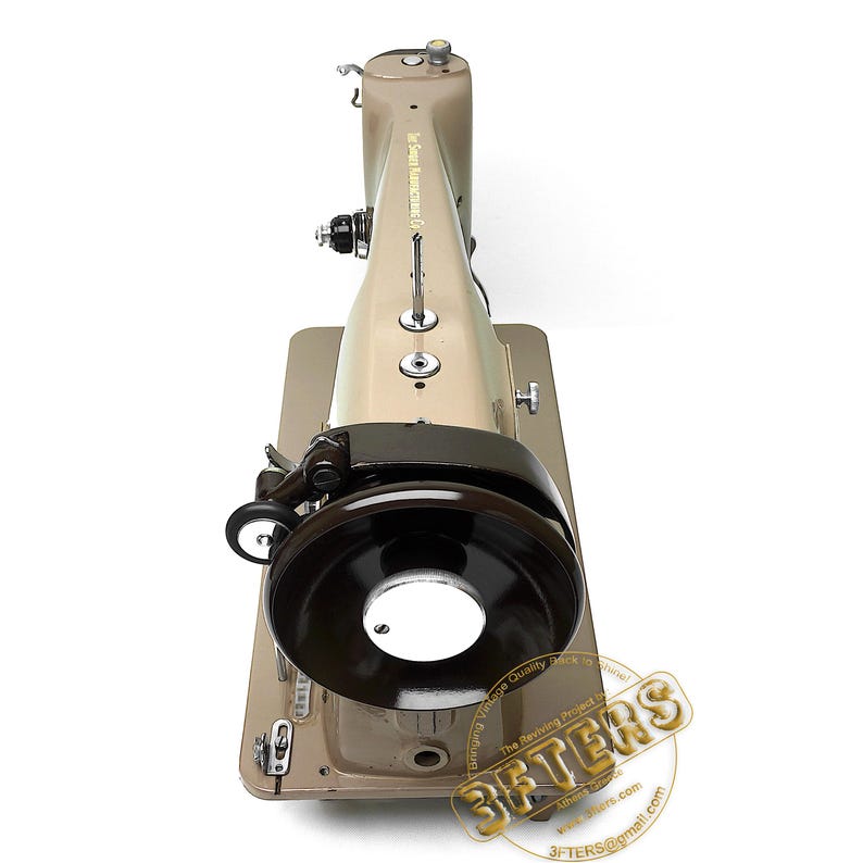 May include: Tan and brown vintage sewing machine with a black wheel and a circular light. The machine has a metallic finish and is set on a rectangular base. The text "3FTERS" is visible on the bottom right.