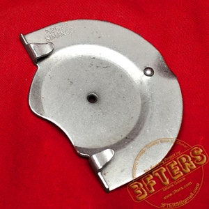 May include: A silver metal part with the text '32622 SIMANCO' printed on it. The part has a hole in the center and a curved edge. The part is on a red surface.