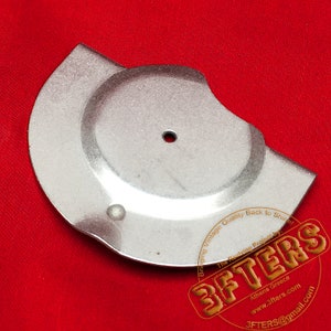 May include: A silver metal disc with a hole in the center and a smaller hole on the side. The disc is on a red surface. The text on the disc reads: 'Bringing Vintage Quality Back to Shirel The Reviving Project by: 3FTERS Athens Greece www.3fters.com 3FTERS@gmail.com'