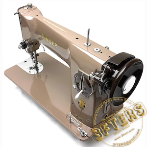 May include: A vintage Singer sewing machine in a tan and brown color scheme. The machine has a shiny, metallic finish and features various dials, levers, and a large black flywheel. The Singer logo is visible on the machine.