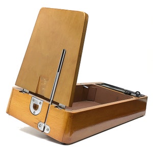 May include: A wooden box with a hinged lid that opens to reveal a compartment inside. The box is made of light brown wood and has a metal latch.