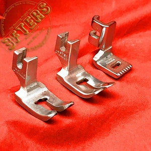 May include: Four silver sewing machine presser feet on a red fabric background. The feet are different sizes and shapes, and they have a variety of markings on them.