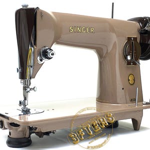 May include: A vintage Singer sewing machine in tan and brown. The machine features the Singer logo in gold lettering, a needle, and various dials and levers. The machine is set on a tan base.