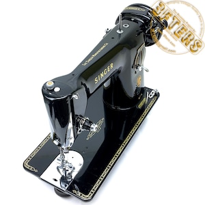 Puede incluir: Una m&aacute;quina de coser Singer negra vintage con detalles dorados. La m&aacute;quina presenta el logotipo de Singer y el texto "The Singer Manufacturing Co.". La base tiene un borde dorado decorativo. La m&aacute;quina est&aacute; sobre un fondo blanco.