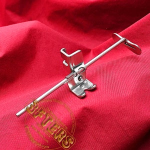 May include: A silver sewing machine foot attachment with a metal rod. The foot is designed to create a rolled hem.