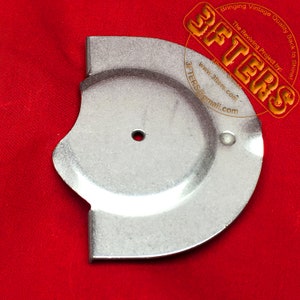 May include: A silver metal part with a circular hole in the center and a curved edge. The part is on a red surface.