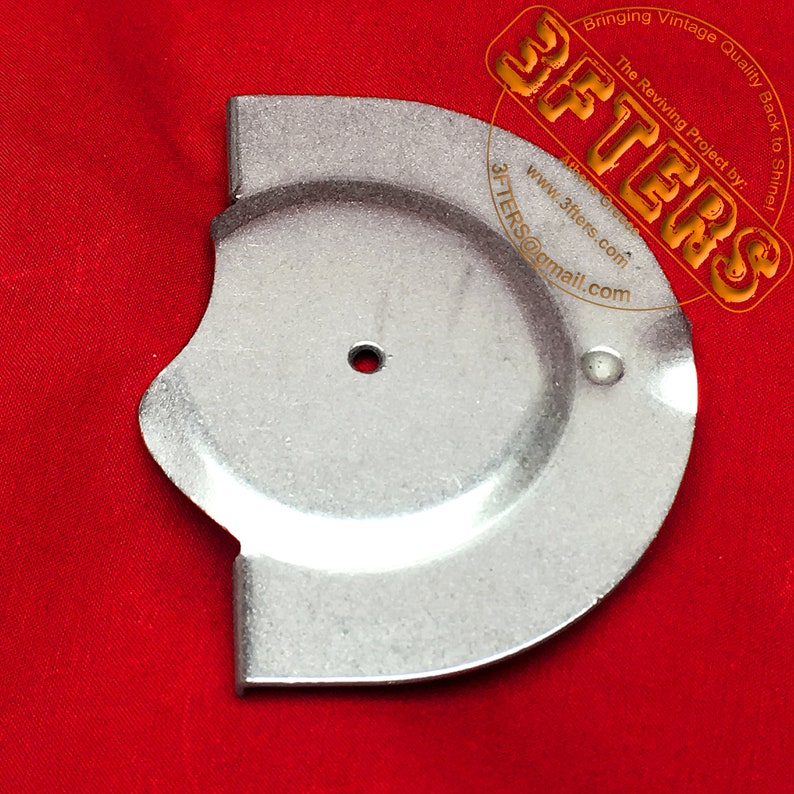 May include: A silver metal part with a circular hole in the center and a curved edge. The part is on a red surface.
