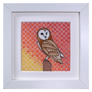 May include: A framed cross-stitch of a barn owl perched on a branch, with a red, orange, and yellow geometric background.