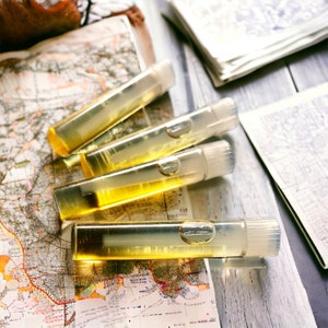 Puede incluir: Cuatro viales rectangulares transparentes llenos de un l&iacute;quido dorado, sobre un mapa antiguo. Los viales tienen tapas blancas y est&aacute;n dispuestos en diagonal. El mapa detalla caracter&iacute;sticas geogr&aacute;ficas y texto, evocando viajes.