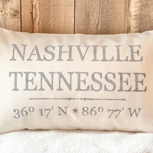 May include: A white pillow with the text "Nashville Tennessee" and the coordinates "36° 17' N * 86° 77' W" printed in gray.