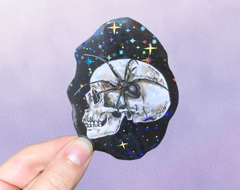 May include: A die-cut sticker featuring a white human skull with a large black spider resting on top. The background is black with a holographic star pattern that reflects light in various colours. The sticker has an irregular, organic shape.