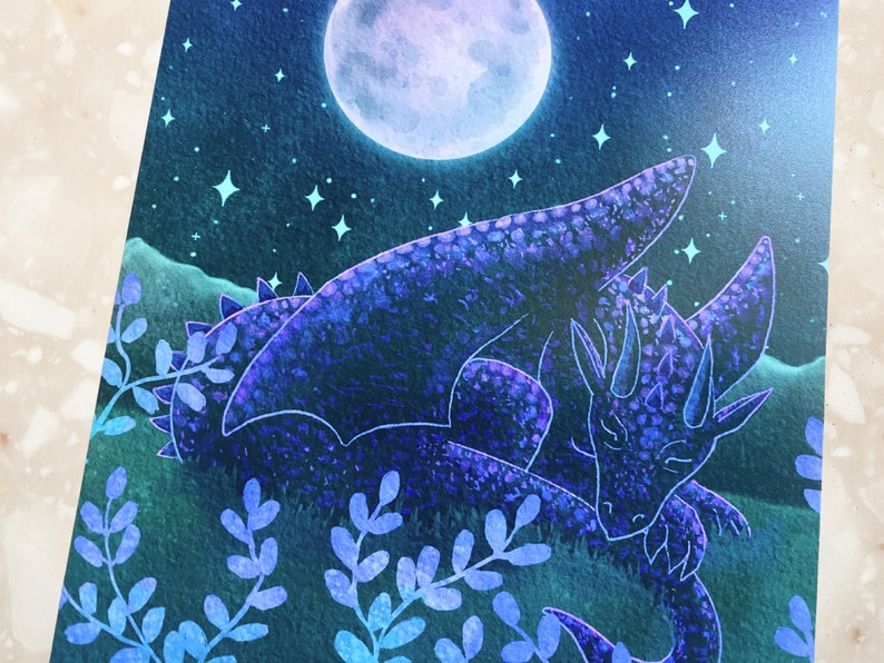 May include: A watercolor painting of a blue dragon sleeping under a full moon with stars in the night sky. The dragon is curled up with its head resting on its wing. The background is a dark blue with hints of green.