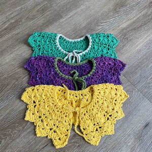 May include: Three handmade crochet collars in shades of green, purple, and yellow. The green collar has a white trim, the purple has a green trim, and the yellow collar has a scalloped edge. Each collar has a tie closure.
