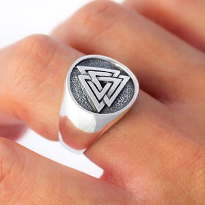 May include: A silver ring with a circular design featuring a three-dimensional, interlocking triangle pattern.