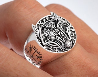 May include: A silver ring with a wolf head design and a compass on the band. The wolf head is detailed with intricate patterns and the compass is surrounded by runes.