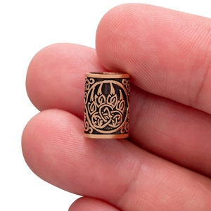Könnte beinhalten: Eine kupferfarbene Metallperle mit einem detaillierten Design einer Bärenpfote, die von einem keltischen Knotenmuster umgeben ist.