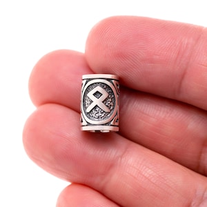 May include: Silver bead with a raised, detailed design of a Norse rune symbol. The bead is cylindrical and has a smooth, polished finish.