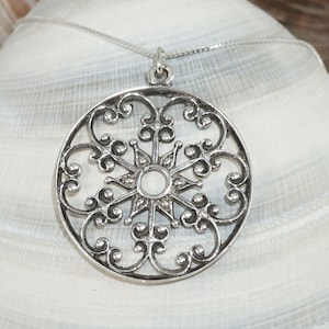May include: A silver pendant necklace with a round, intricate, filigree design. The pendant features a circular center with a starburst pattern.