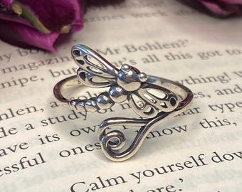 May include: A silver ring featuring a dragonfly design with intricate details. The ring is adjustable and has a delicate, openwork design.