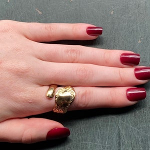 May include: A gold-toned spoon ring featuring an open-ended design. The band is crafted from the handle of a spoon, showcasing an embossed floral pattern on the wider end and a smooth, rounded finish on the narrower, tapering end.