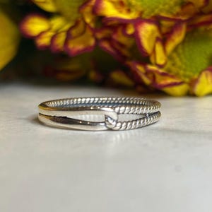 May include: A silver ring with a twisted rope design. The ring is made of two bands that are intertwined.