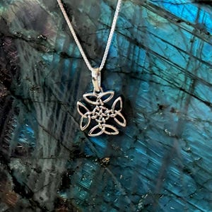 May include: A silver pendant necklace featuring a Celtic knot design. The pendant is a symmetrical, openwork design with four interconnected loops surrounding a central knot. The necklace chain is a delicate silver box chain. The background is a blue and green stone.