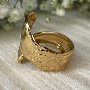May include: A gold-toned ring crafted from a repurposed spoon, featuring an open-ended design. The band displays a detailed, embossed floral pattern along its exterior surface, with the curved handle of the spoon forming the ring's structure.