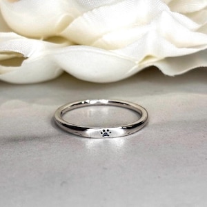 May include: A silver ring with a small paw print design. The ring is thin and has a polished finish. The paw print is centered on the front of the ring. The ring is likely made of sterling silver.