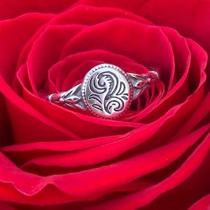 May include: A silver ring with a floral design sits inside a red rose.