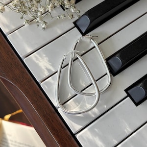 May include: Silver oval hoop earrings on a white and black piano keyboard.