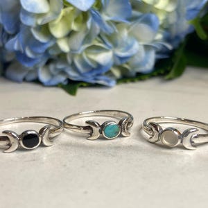 May include: Three silver rings with a triple moon design. Each ring features a different colored stone: black, turquoise, and white.
