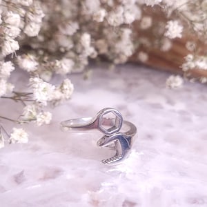 May include: A silver ring shaped like a wrench. The ring is on a white background.