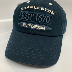 May include: A dark blue baseball cap with white embroidery that reads "Charleston Est 1670 South Carolina".