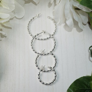 May include: Three pairs of silver hoop earrings with a beaded design. The earrings are stacked on top of each other, with the largest pair at the top and the smallest pair at the bottom.