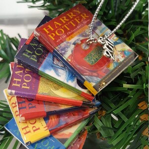May include: A Christmas ornament featuring a stack of miniature Harry Potter books with the title "Harry Potter and the Philosopher's Stone" visible on the top book. The ornament is decorated with a silver charm that reads "2019".