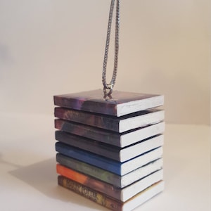 May include: A stack of miniature Harry Potter books with white covers, each with a different colored spine, hanging from a silver chain. The bottom book reads "Harry Potter and the Sorcerer's Stone".