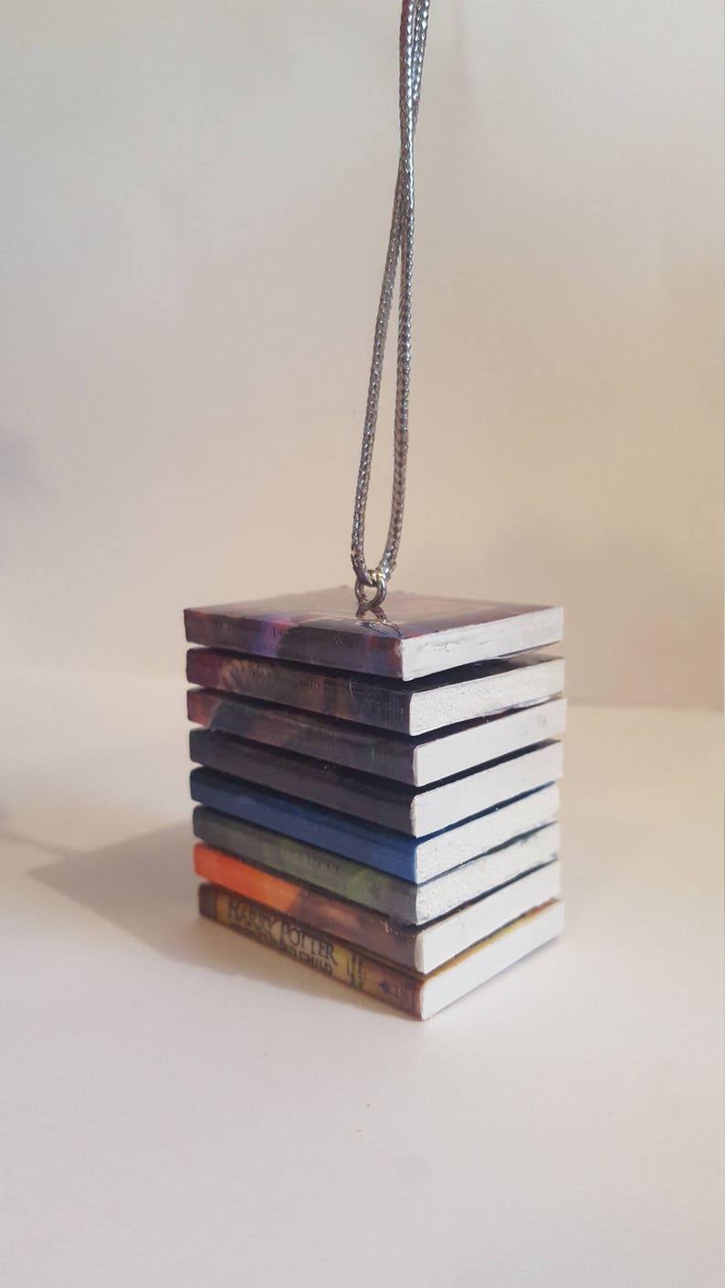 May include: A stack of miniature Harry Potter books with white covers, each with a different colored spine, hanging from a silver chain. The bottom book reads "Harry Potter and the Sorcerer's Stone".