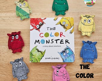 May include: A square children's book titled The Color Monster by Anna Llenas, surrounded by eight felt monster cutouts in various colors including red, yellow, green, blue, pink, gray, and teal, arranged on a light wood surface.
