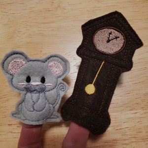 May include: Two felt finger puppets: a gray mouse with pink accents and a brown grandfather clock with a beige clock face. The mouse has a pink embroidered nose and ears. The clock has a yellow pendulum.