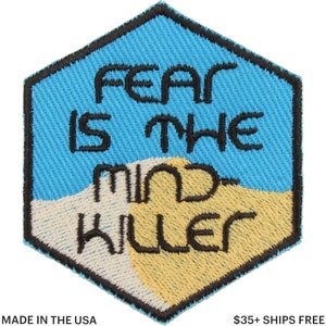 May include: Hexagonal embroidered patch with the text "FEAR IS THE MIND KILLER" in black. The patch has a light blue background with tan and off-white sections. The border is black.