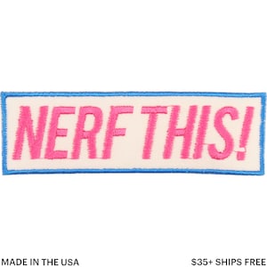 May include: Embroidered patch with the text "NERF THIS!" in bright pink, set against an off-white background. The patch is bordered by a thin blue line, with the words "MADE IN THE USA" at the bottom.