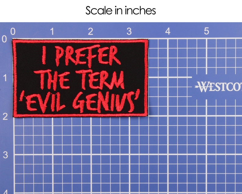 May include: Black rectangular patch with red embroidered text: "I PREFER THE TERM 'EVIL GENIUS'". The patch is approximately 4 inches wide and 2 inches tall. The patch is on a blue grid background with a ruler.