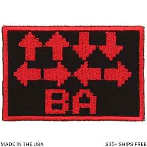 May include: Black rectangular patch with red embroidered arrows pointing up, down, left, and right. The letters "BA" are below the arrows. The patch has a red border. The text "MADE IN THE USA" is at the bottom.