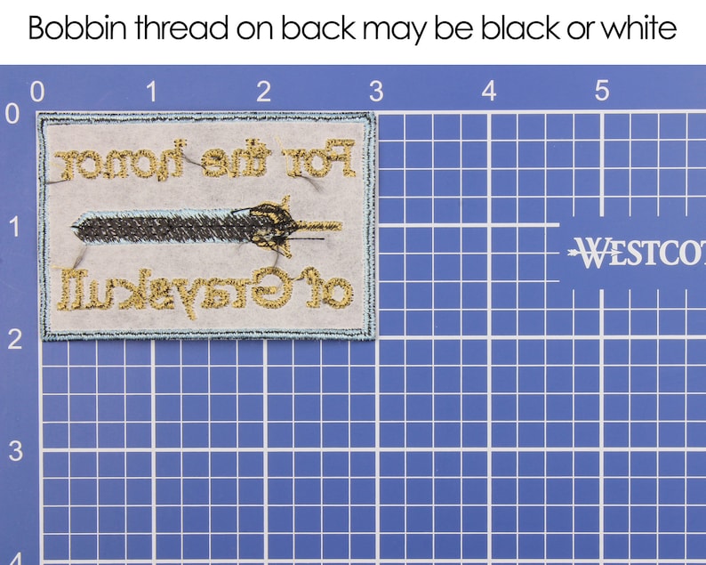 May include: Embroidered patch with the text "For the Honor of Greyskull" and a sword design. The patch has gold and black thread on a light gray background with a teal border. The bobbin thread on the back may be black or white.