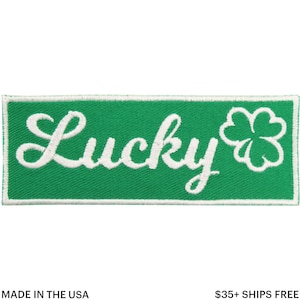 May include: A green rectangular patch with white embroidered text that reads "Lucky" and a four-leaf clover. The patch has a white border and is made in the USA.