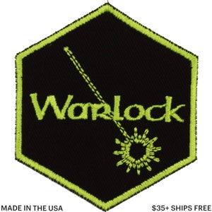 May include: Black hexagonal patch with a neon green border and accents. The word "Warlock" is embroidered in neon green, along with a stylized design of a starburst and a dotted line. The text "MADE IN THE USA" is at the bottom.