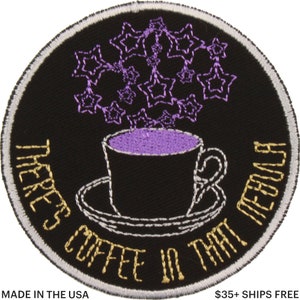May include: Embroidered patch with a black background, featuring a coffee cup and saucer. The cup is filled with purple liquid, and a cluster of purple stars floats above it. The text "THERE'S COFFEE IN THAT NEBULA" is embroidered around the edge in gold.
