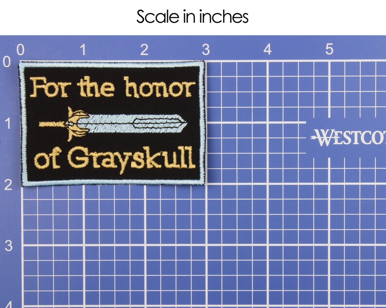 May include: Black rectangular patch with gold embroidered text reading "For the honor of Grayskull." A light blue sword design is centered on the patch. The patch is approximately 2 inches by 3 inches.